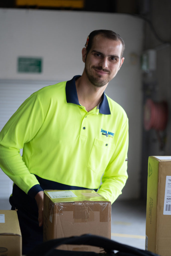 Man wearing a high vis top smiling at the camera holding a box